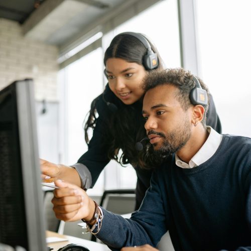 Two call center employees working together with headsets in a modern office setting.